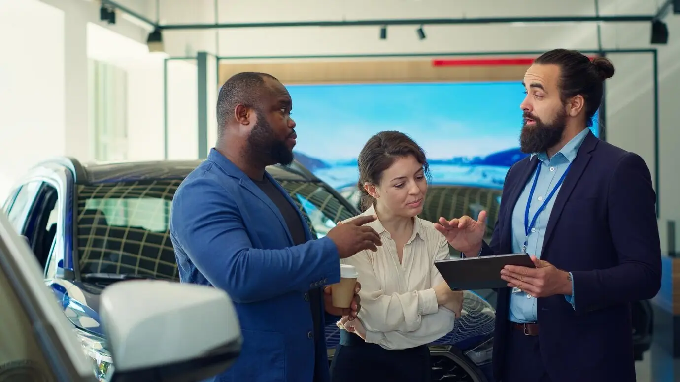 Продавец автосалона демонстрирует клиентам ассортимент на планшете.