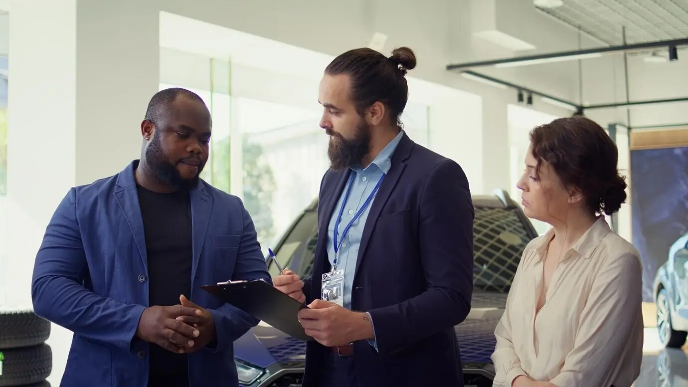 Дружелюбный продавец автомобилей демонстрирует клиентам автомобили автосалона.